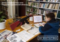 A child reading books on the AK-47 and other weaponry beneath a sign that reads "Mikhail Kalashnikov — Weapons Genius." The image was captured in a children's library in the village of Perelyub in Russia's Saratov Region / Source: Agentstvo